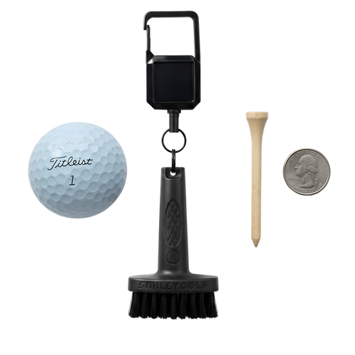 A golf club cleaning brush kit on a white background, including the SMILEY GOLF Mini Golf Brush with a Clip, a Titleist golf ball, a wooden tee, and a US quarter for scale.